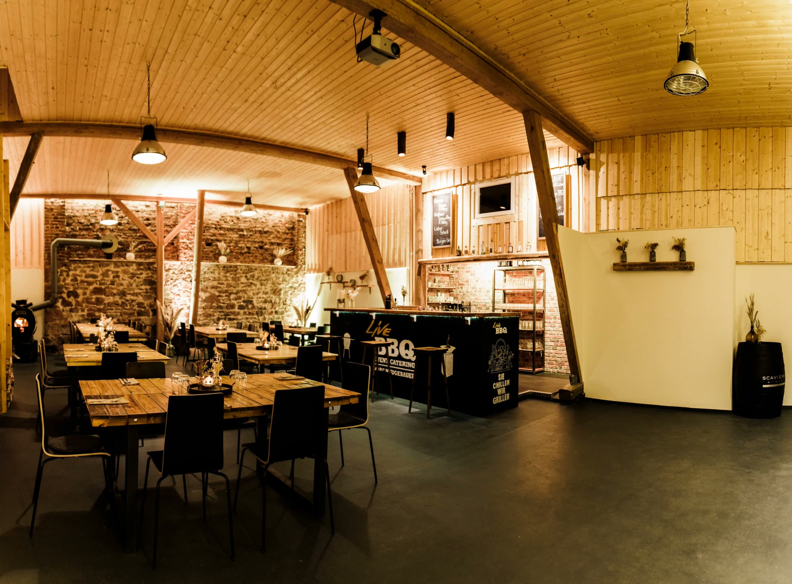 Die Eventscheune von LiveBBQ mit Holzdecke, Natursteinwand, Tischen und Bar