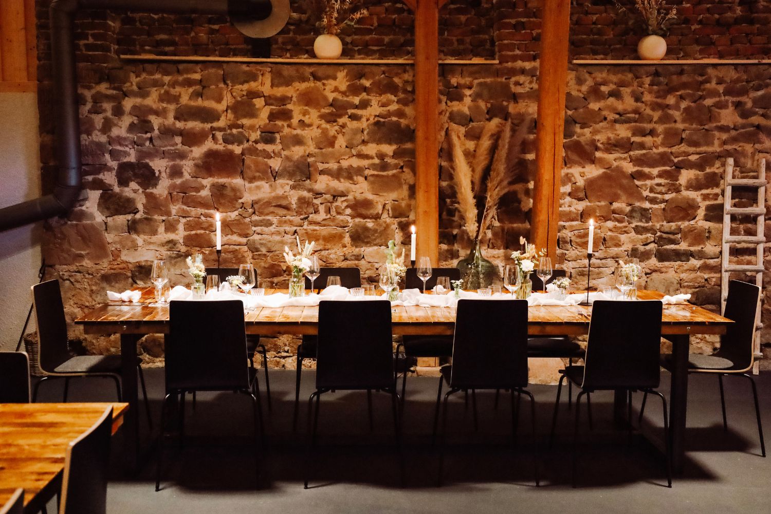 Lange, festlich gedeckte Tafel mit Kerzen vor einer Natursteinwand bei LiveBBQ